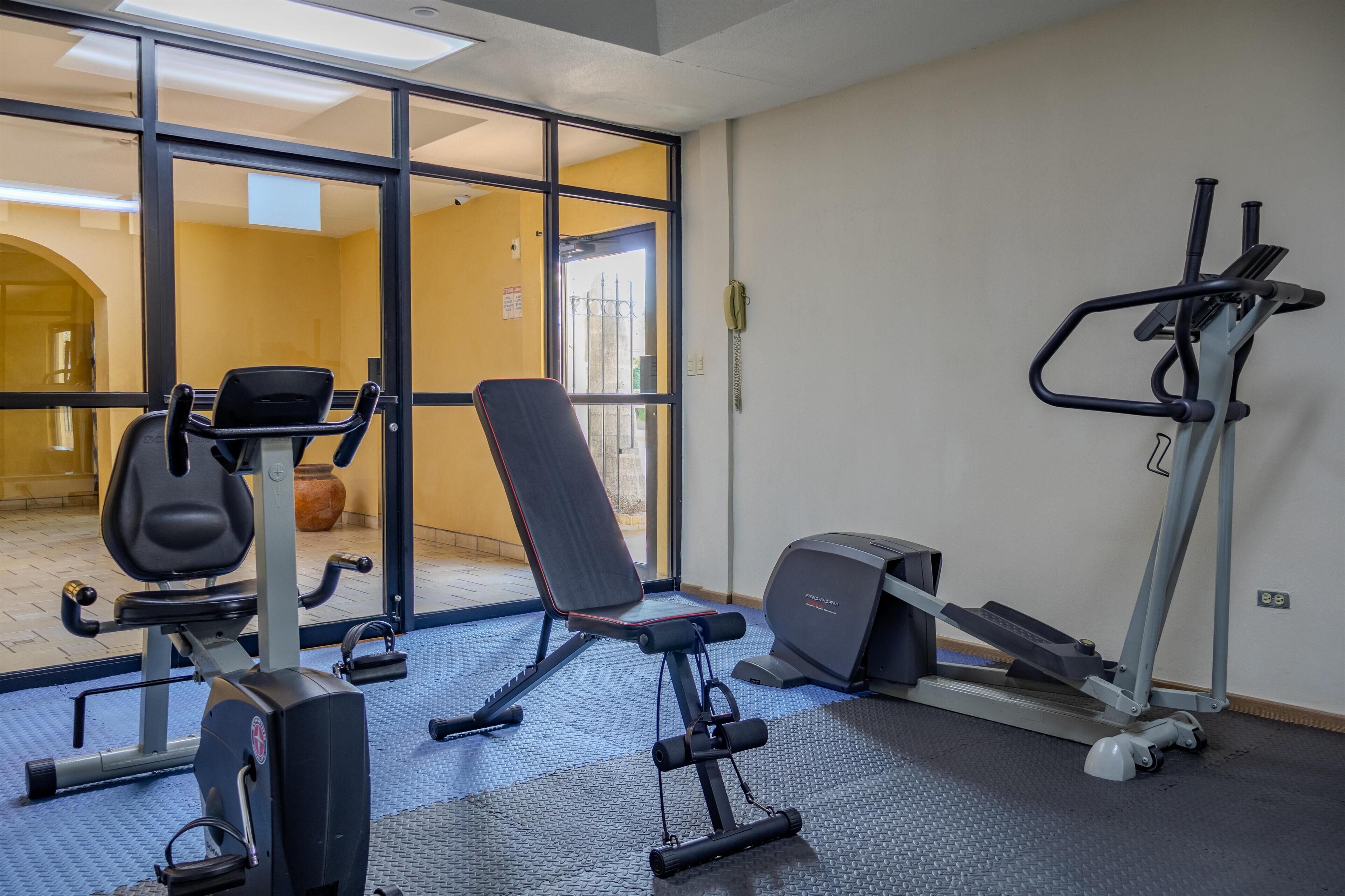 Une salle de sport équipée de matériel d’exercice, d’un banc et d’un tapis de course.