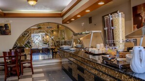 A hotel breakfast area with a buffet setup, including a coffee machine, cereal dispensers, and a seating area with chairs. - Best Western Hotel Plaza Matamoros (Matamoros)