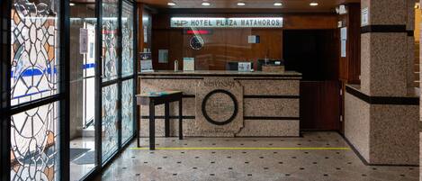 A hotel reception area with a reception desk, a clock, and a sign that reads "LP Hotel Plaza Matamoros".