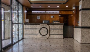 Zona de recepción de un hotel, con mostrador de mármol, un reloj y un letrero que dice "Hotel Plaza Matamoros".