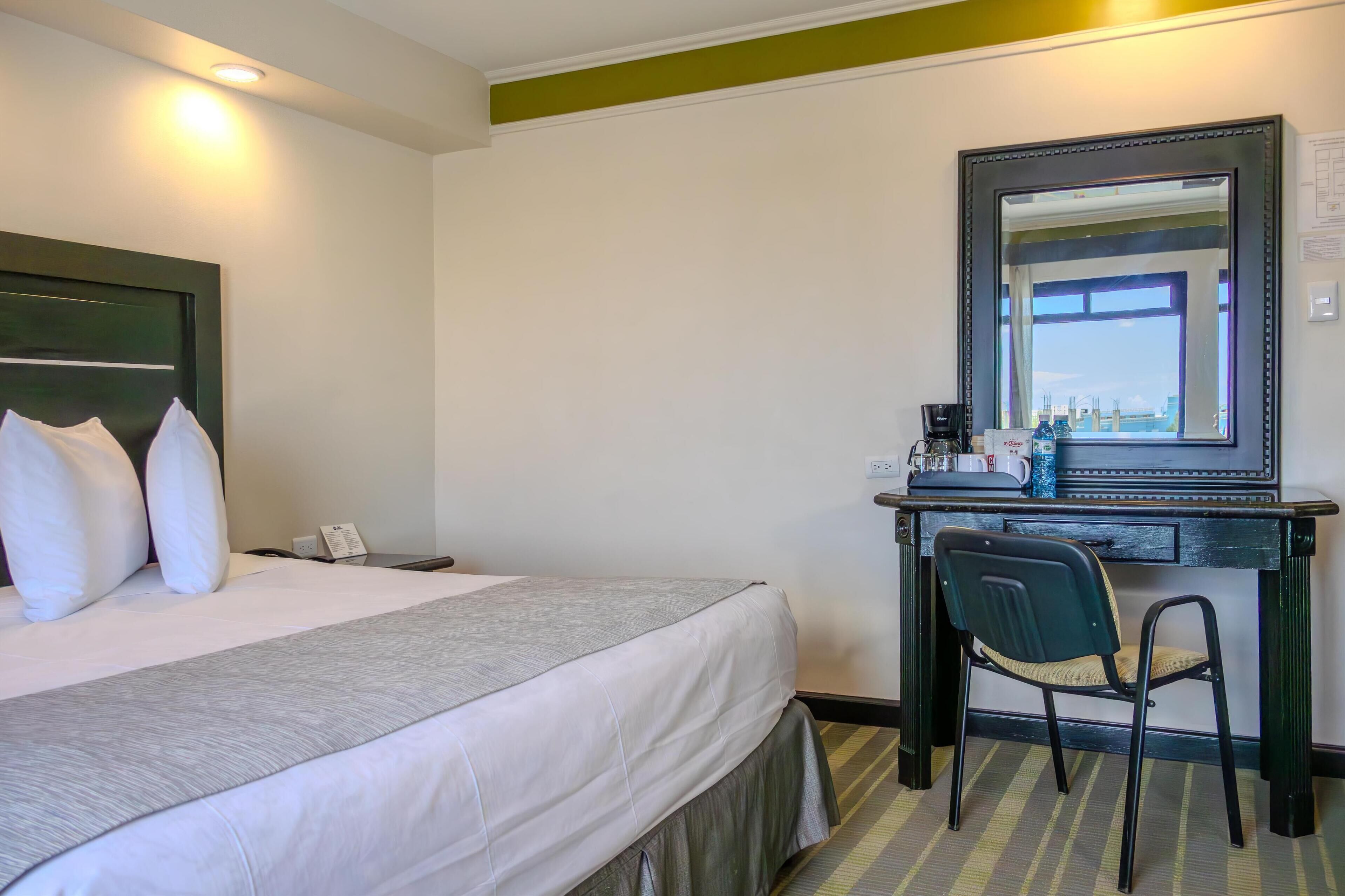 A hotel room with a bed, a desk, a chair, and a large mirror.