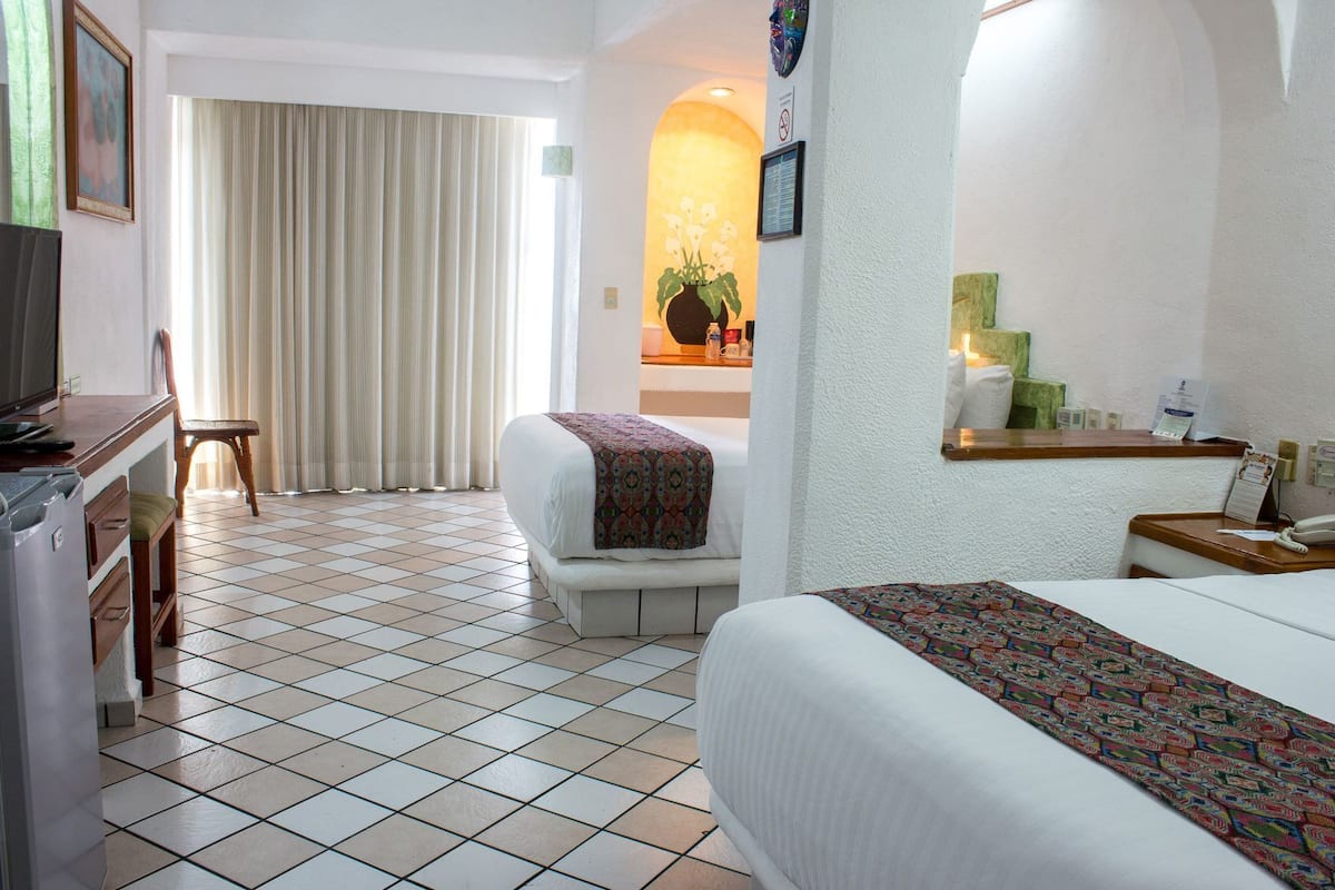 Una camera d'hotel con un letto, una sedia, una scrivania, una televisione, uno specchio e una finestra con tende.