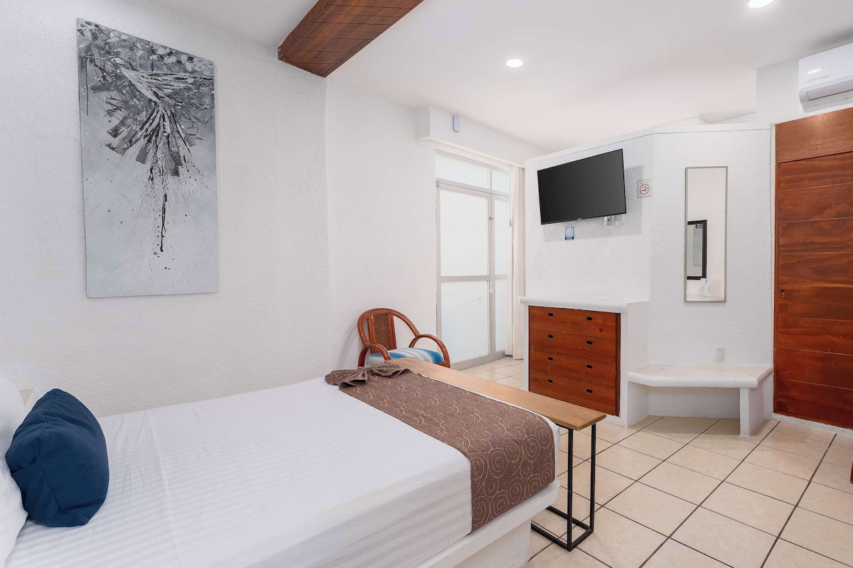 Una camera d'albergo con un letto, una scrivania, una sedia, una televisione e un armadio.