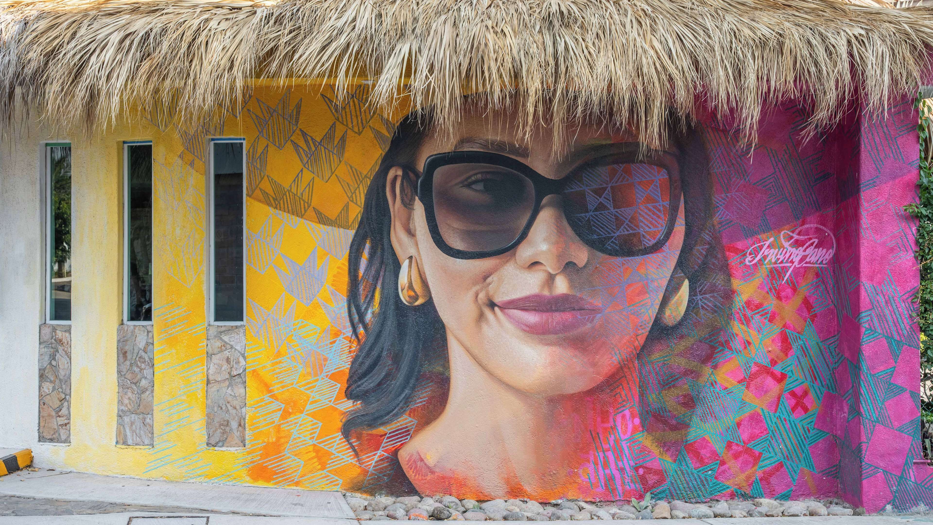 A mural with geometric patterns and a tropical thatched roof.