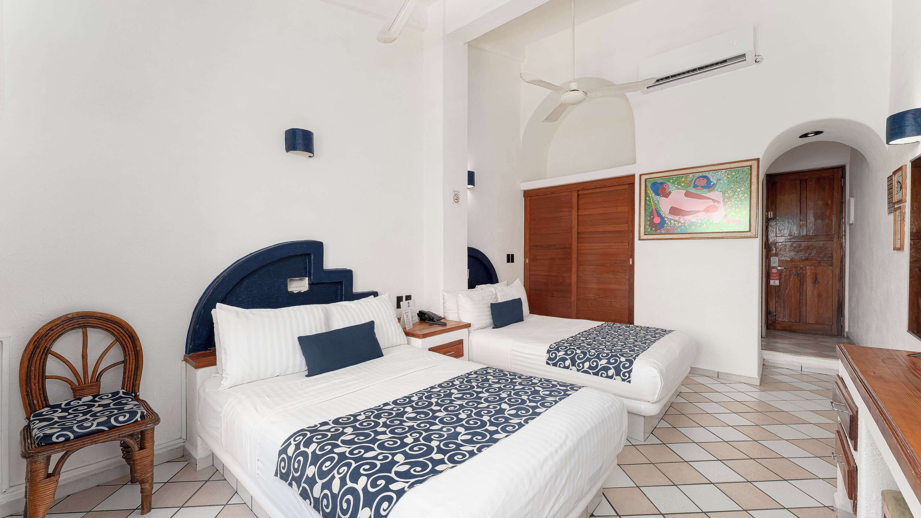 A hotel room with two beds, a wooden chair, a wooden desk, a wardrobe, and a door.