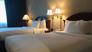 A hotel room with two beds, each with white bedding and pillows, a nightstand with a phone and a lamp, and wall-mounted lamps. - The Marx Hotel (Oneonta)