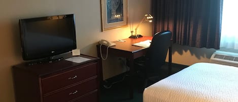 Ein Hotelzimmer mit zwei Betten, einem Schreibtisch mit Computer und Telefon, einem Fernseher und einem gerahmten Bild an der Wand.