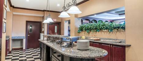 A hotel kitchen with granite countertops, stainless steel appliances, and a checkered floor.