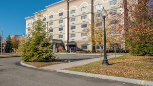 A multi-story hotel with a central entrance, a covered outdoor seating area, and a well-maintained landscaped area with trees and a street lamp. - The Marx Hotel (Oneonta)