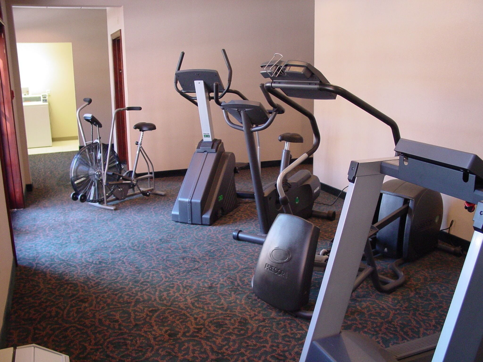 Ginásio de hotel com bicicletas ergométricas, esteira e máquina de remo.
