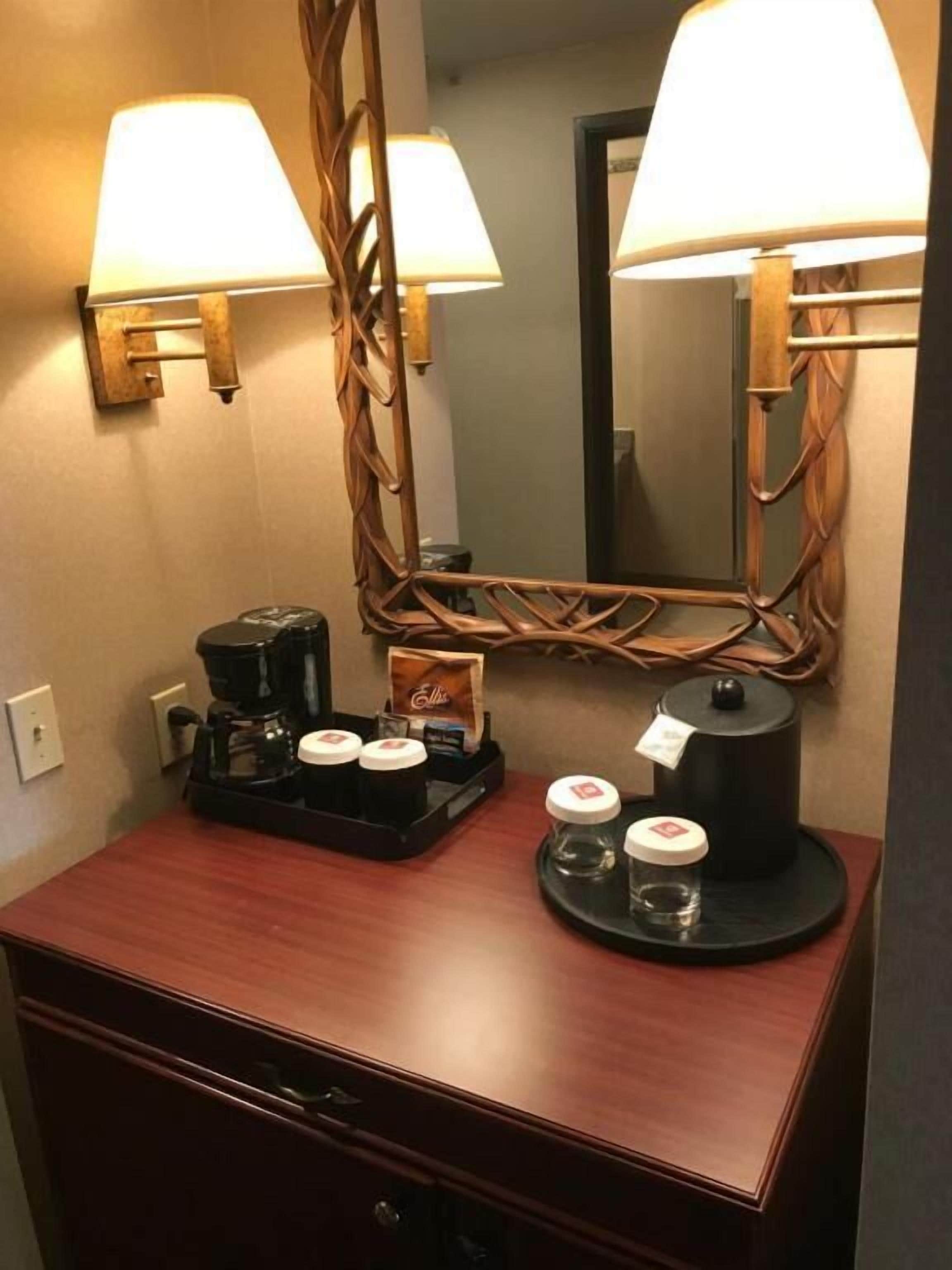 A hotel room with a wooden desk, a coffee maker, and two lamps.
