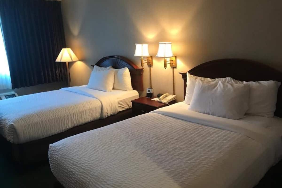 A hotel room with two beds, a nightstand with a phone, and wall-mounted lamps.