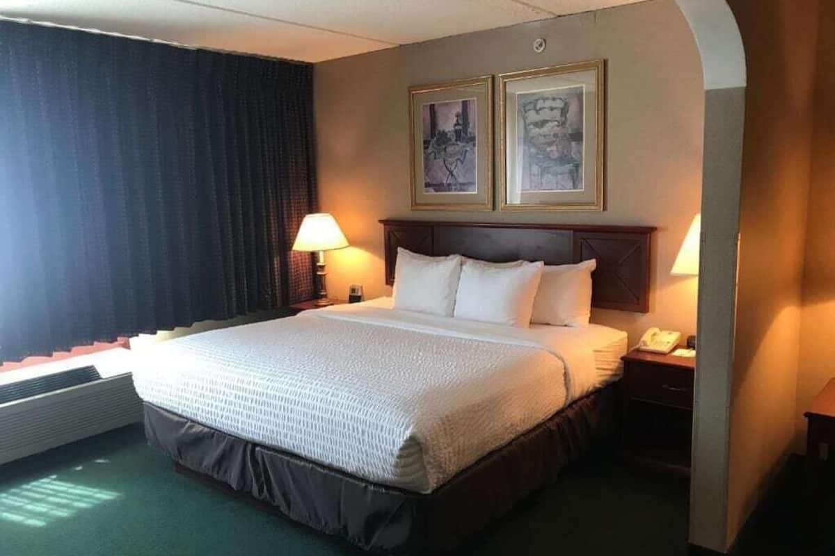 A hotel room with a large bed, two bedside lamps, a telephone, and two framed pictures on the wall.