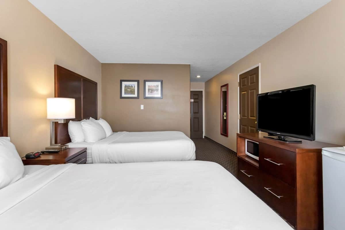 Habitación de hotel con dos camas, un televisor, una lámpara y una puerta que da a otra habitación.