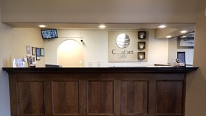 Un mostrador de recepción con paneles de madera, un televisor montado y un cartel que dice "Comfort Inn".