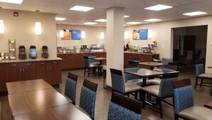 Un comedor con varias mesas y sillas, una cocina equipada y una barra con dispensadores de café.