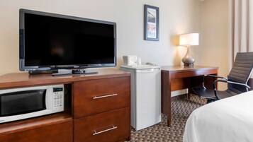 Habitación de hotel con televisión de pantalla plana, microondas, refrigerador pequeño, escritorio con lámpara, una silla y una cama.
