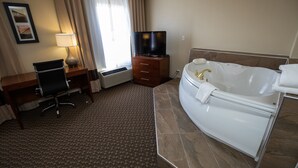 Habitación de hotel con escritorio, silla, televisor y una bañera grande.