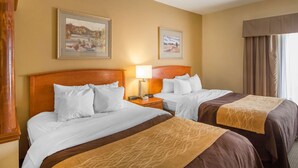 A hotel room with two beds, a wooden headboard, a nightstand, a lamp, and two framed pictures on the wall.
