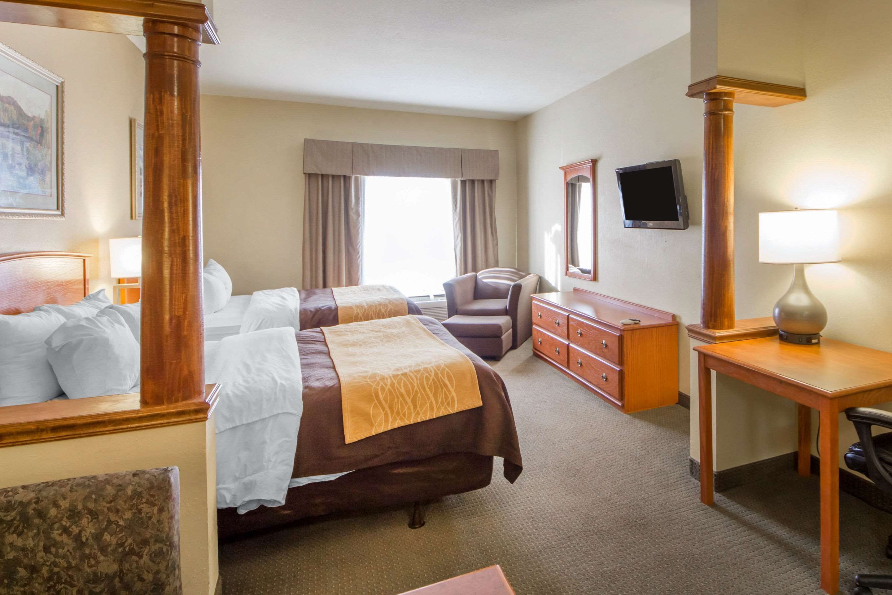 A hotel room with two beds, a desk, a chair, a dresser, a television, and a window with curtains.