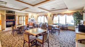 A hotel lobby with multiple dining tables and chairs, a fireplace, and large windows with curtains. - Quality Inn & Suites MidAmerica Industrial Park Area (Pryor)