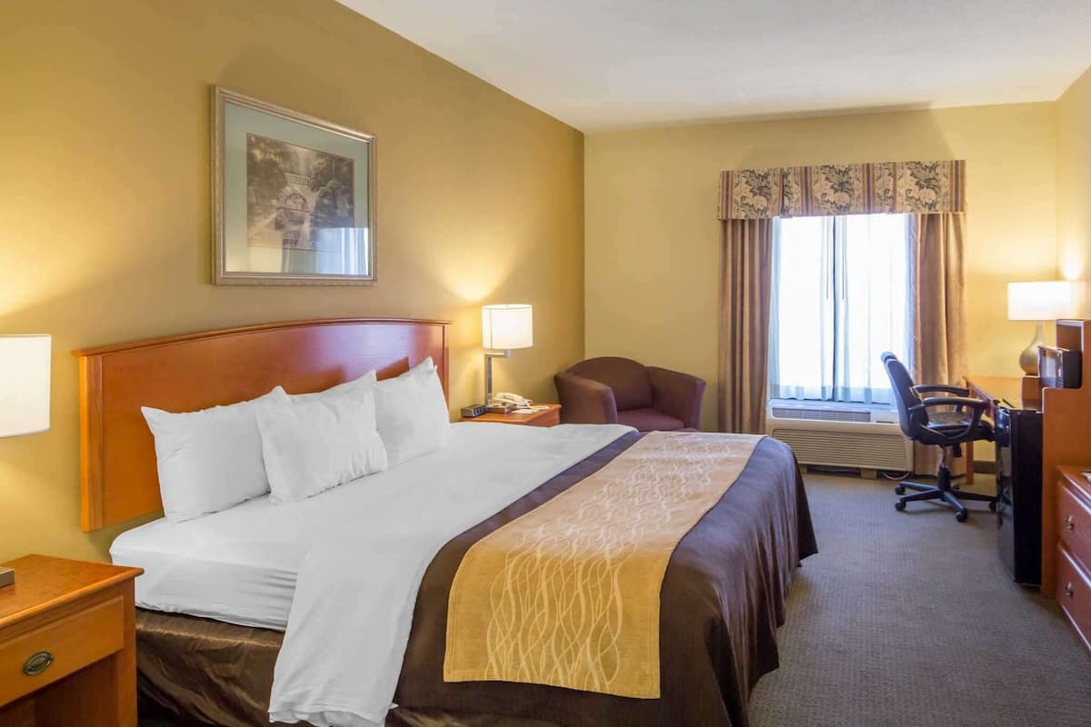 A hotel room with a large bed, a desk, a chair, and a window with curtains.