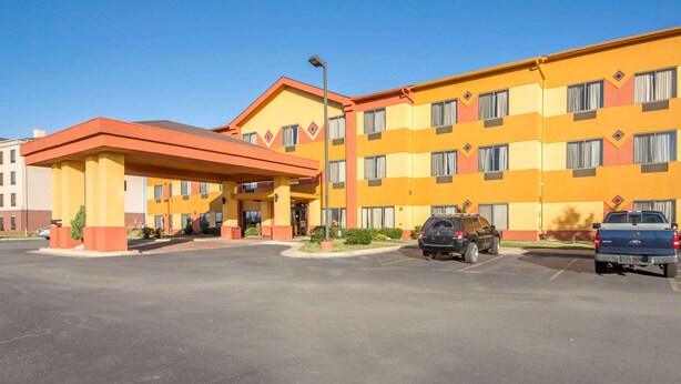 A multi-story hotel with a yellow facade and a red roof. There are two parking spaces visible with a black car and a blue truck parked.
