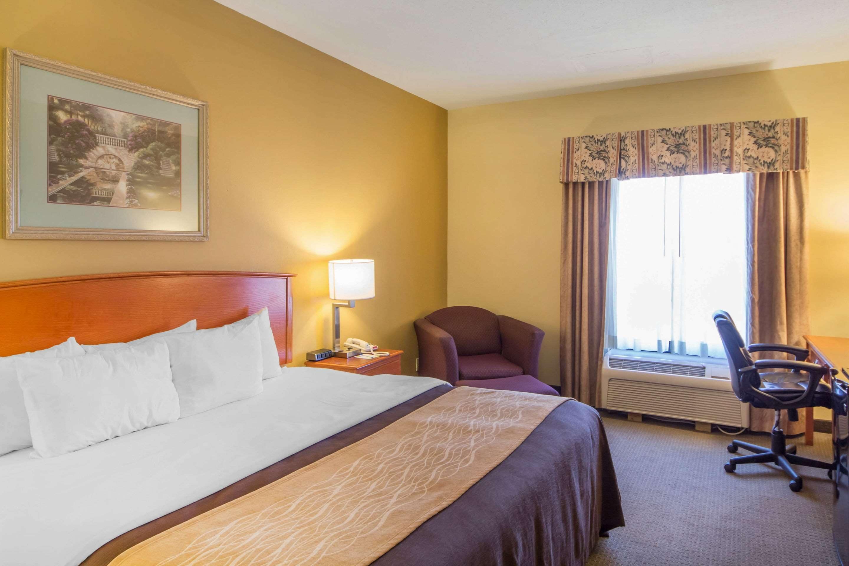 Una habitación de hotel con una cama grande, un escritorio, una silla, una lámpara y una ventana con cortinas.
