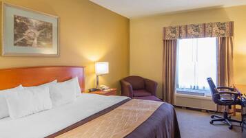 Una habitación de hotel con una cama grande, un escritorio, una silla, una lámpara y una ventana con cortinas.