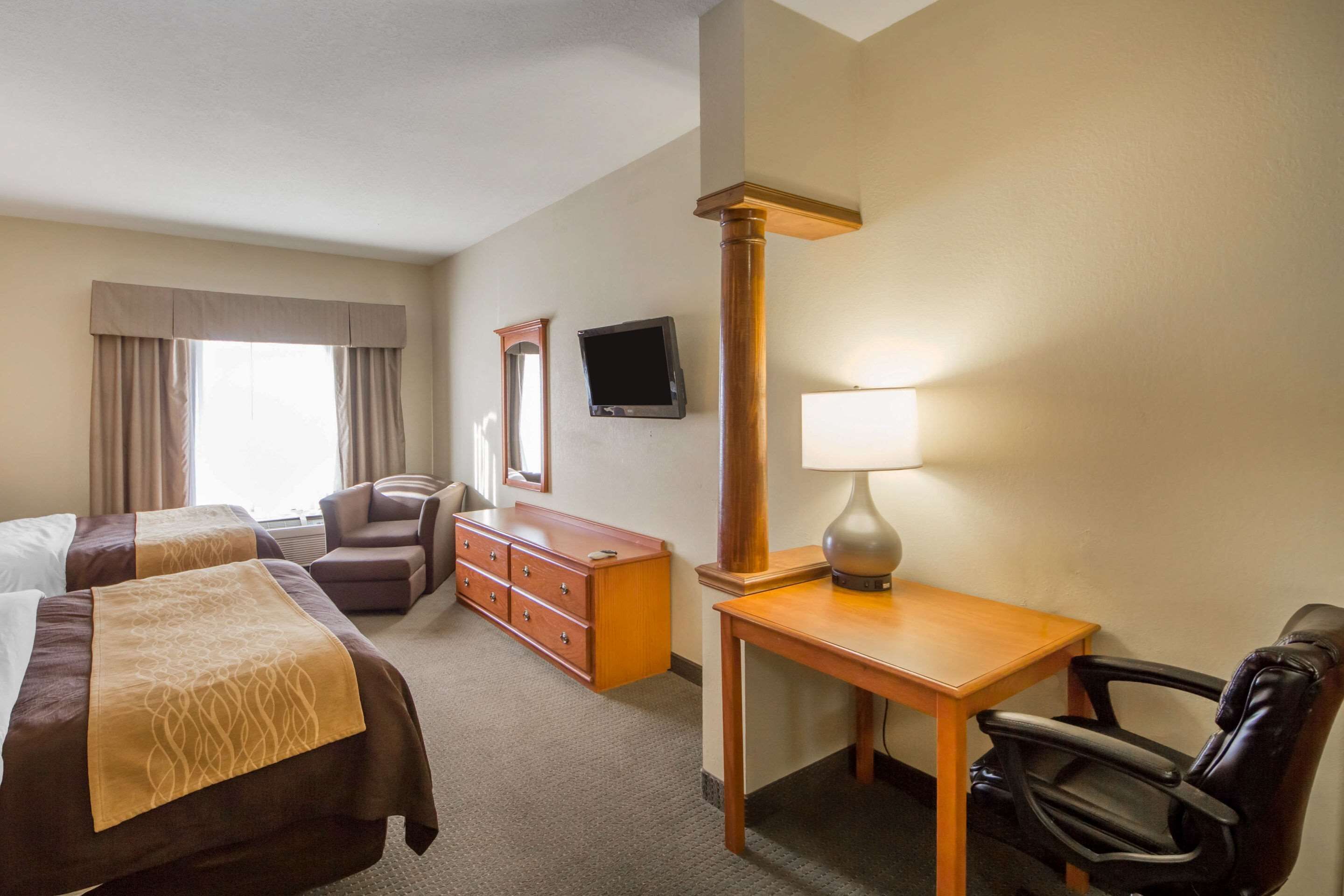 A hotel room with two beds, a desk, a chair, a dresser, a lamp, a television, and a window with curtains.