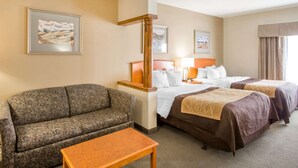 A hotel room with a sofa, two beds, a wooden table, and framed artwork on the walls. - Quality Inn & Suites MidAmerica Industrial Park Area (Pryor)