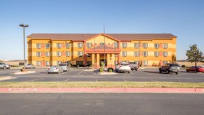 A multi-story hotel with a central entrance, a parking lot with several cars, and a 'No Parking Fire Lane' sign.