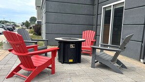 Espace extérieur aménagé avec des fauteuils Adirondack et une table ronde, le tout installé devant un bâtiment doté d’une grande fenêtre.
