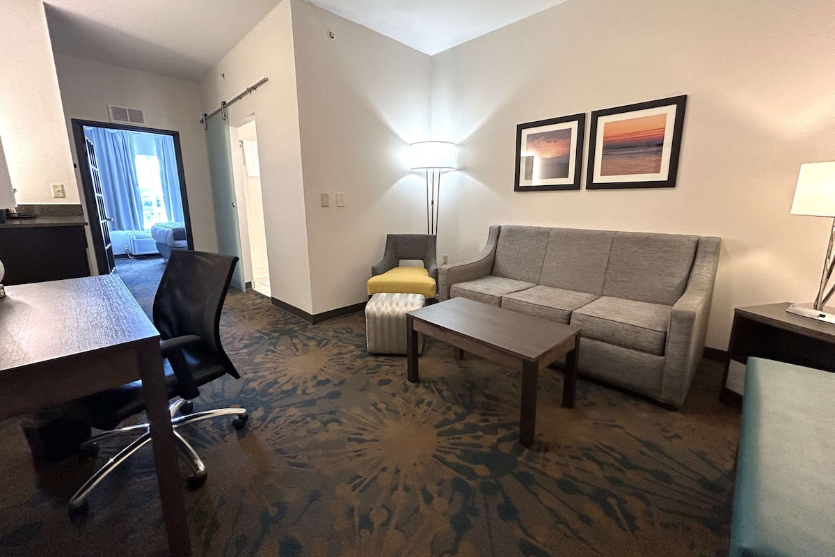 A hotel room with a sofa, a coffee table, a desk, a chair, and two framed pictures on the wall.