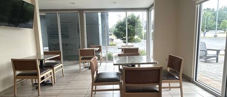 Un amplio comedor interior con varias mesas y sillas, ventanas grandes que ofrecen vistas al exterior y un televisor de pantalla plana montado en la pared.