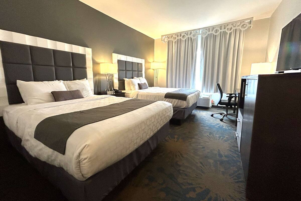 A hotel room with two beds, a desk, a chair, and a television.