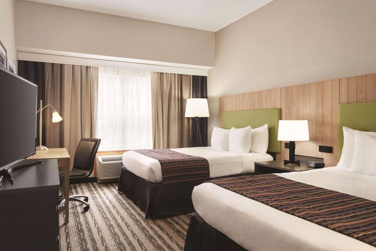 Habitación de hotel con dos camas, un escritorio, un televisor y una ventana con cortinas.