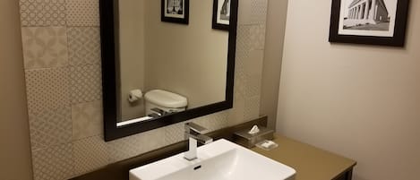 A bathroom with a large mirror, a white sink, and patterned tiles on the walls.