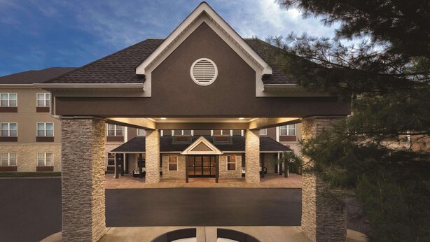 A hotel entrance with a covered patio area, stone pillars, and a circular seating arrangement.