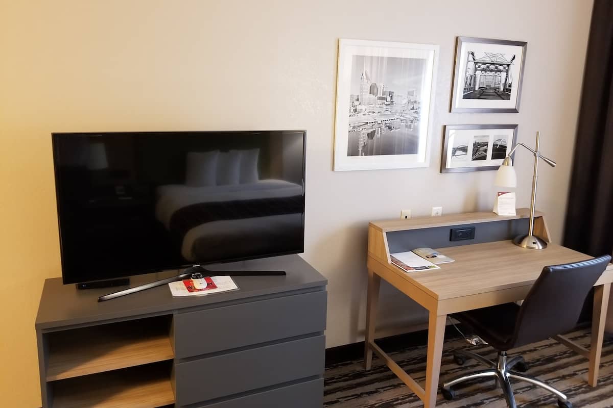 Una habitación de hotel con cama, escritorio y silla, televisor y cuadros en la pared.