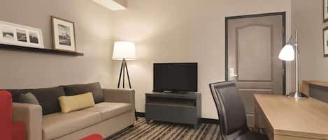 A hotel room with a sofa, a TV, a desk, a chair, and a lamp.