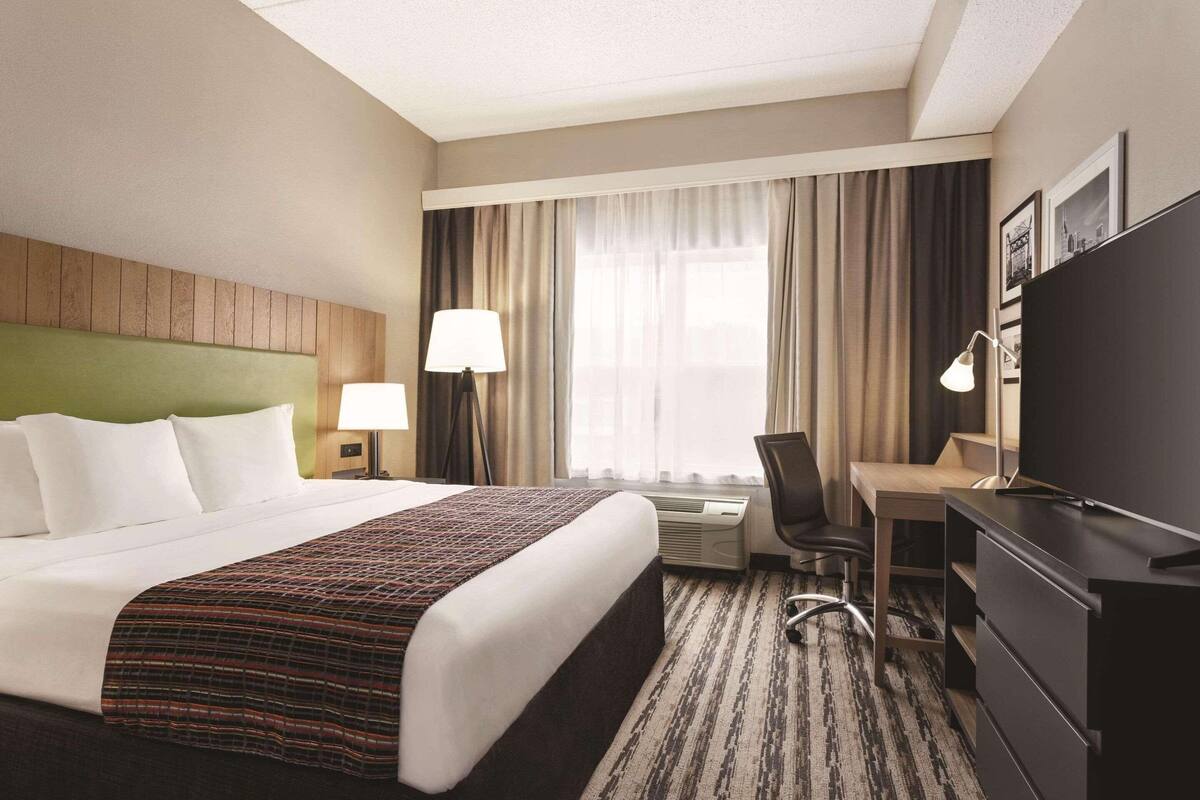 Habitación de hotel con cama, escritorio, silla, televisor y cortinas.