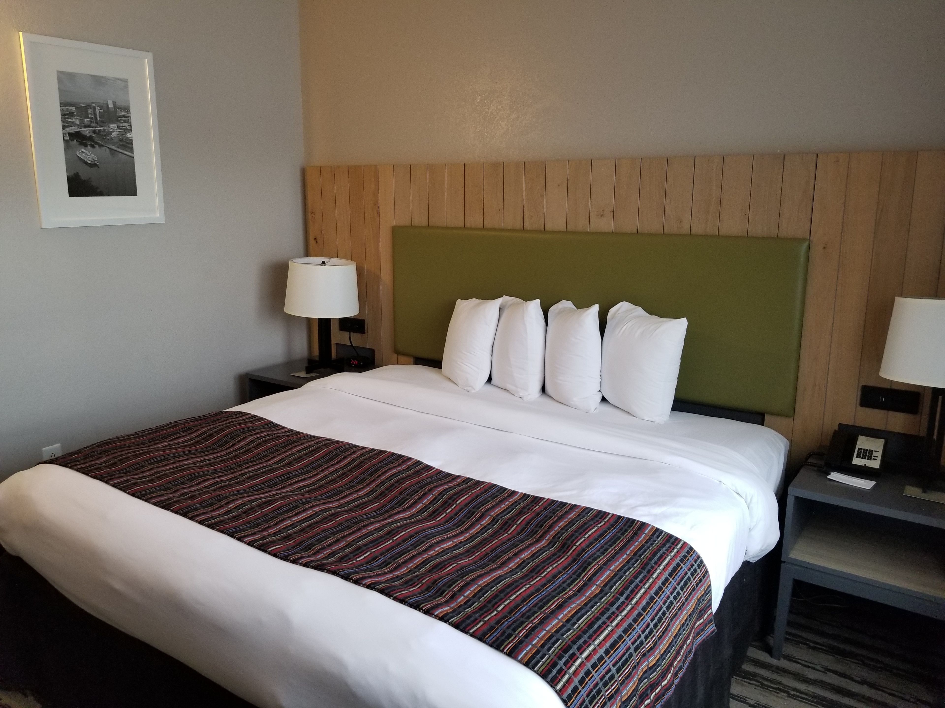 Una habitación de hotel con una cama grande, un cabecero de madera, ropa de cama blanca y dos mesitas de noche con lámparas.