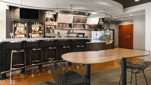 A modern bar area with a wooden table and bar stools, a menu board, and a variety of liquor bottles. - Courtyard by Marriott El Paso Airport (El Paso)