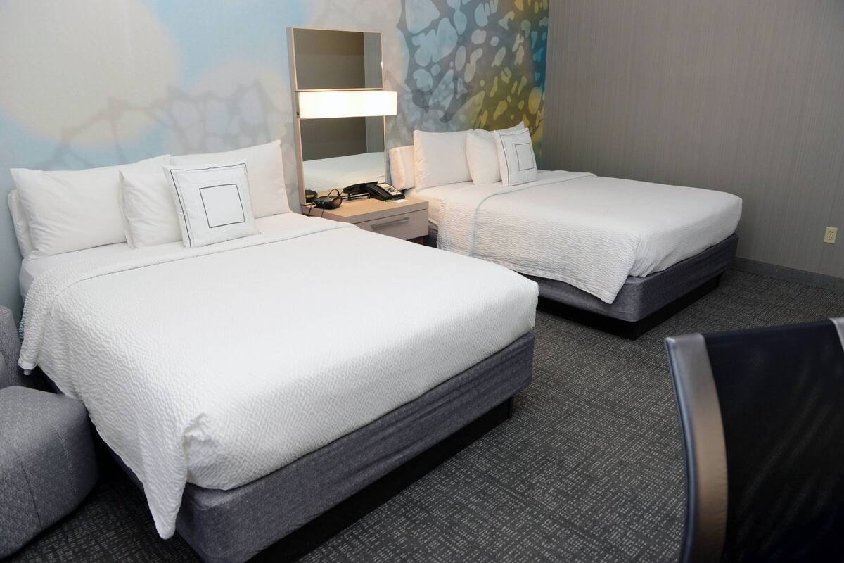 Una habitación de hotel con dos camas, una mesita de noche con lámpara, teléfono y espejo.