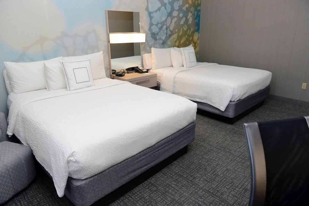 Una habitación de hotel con dos camas, una mesita de noche con lámpara, teléfono y espejo.