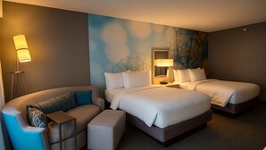 A hotel room with a curved sofa, a small table, two beds, and a wall with a textured design. - Courtyard by Marriott El Paso Airport (El Paso)