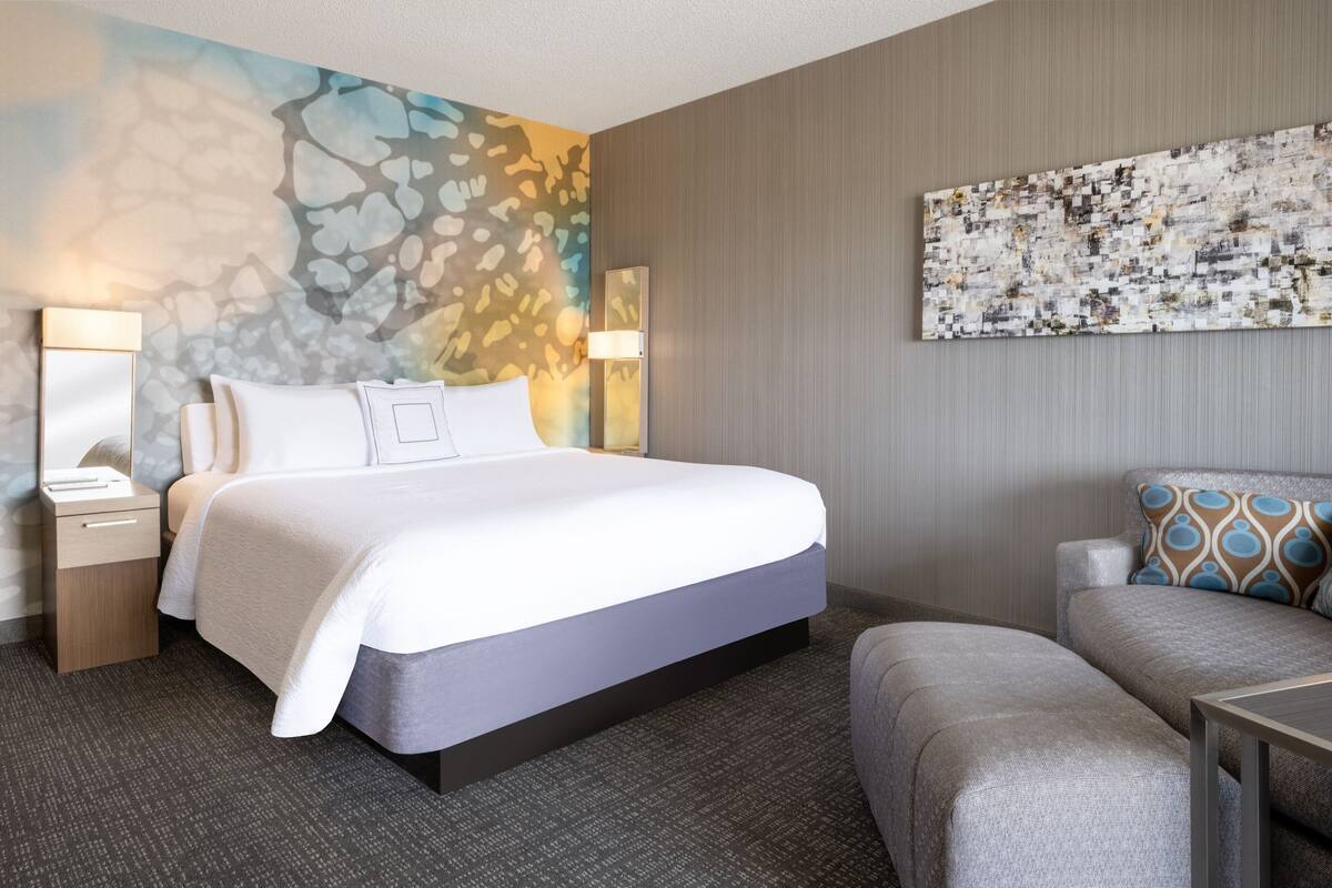 Una habitación de hotel con una cama grande, un sofá, un escritorio y una pared decorada con arte abstracto.