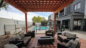 An outdoor patio area with wicker furniture and a fire pit, overlooking a swimming pool and adjacent buildings. - Courtyard by Marriott El Paso Airport (El Paso)