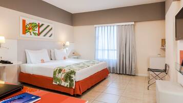 A hotel room with a bed, a desk, a chair, a TV, and a window with curtains.